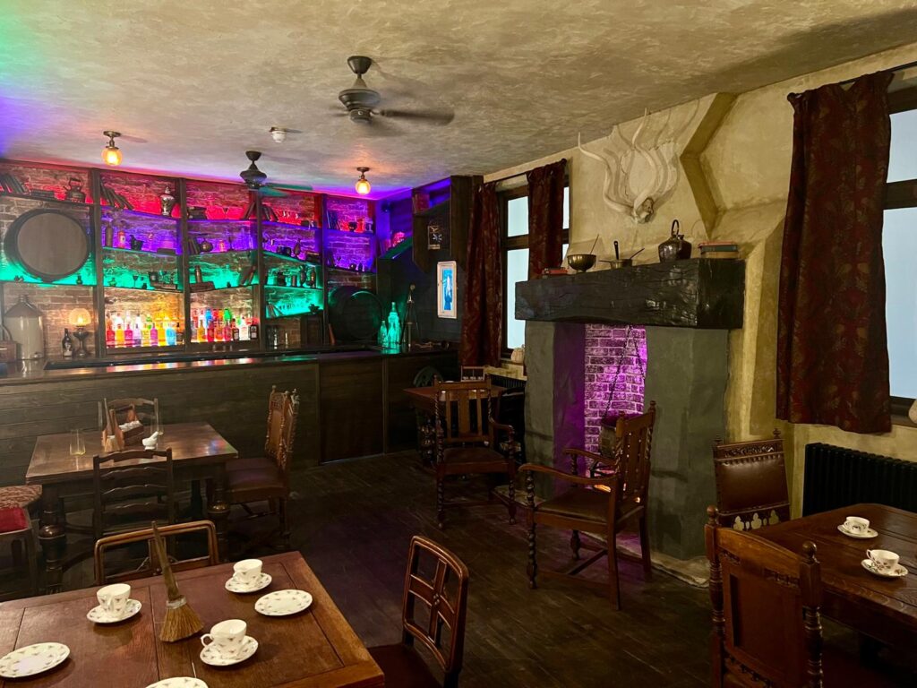 Tables, the colourful bar and the cauldron fireplace inside The Twisted Broom.