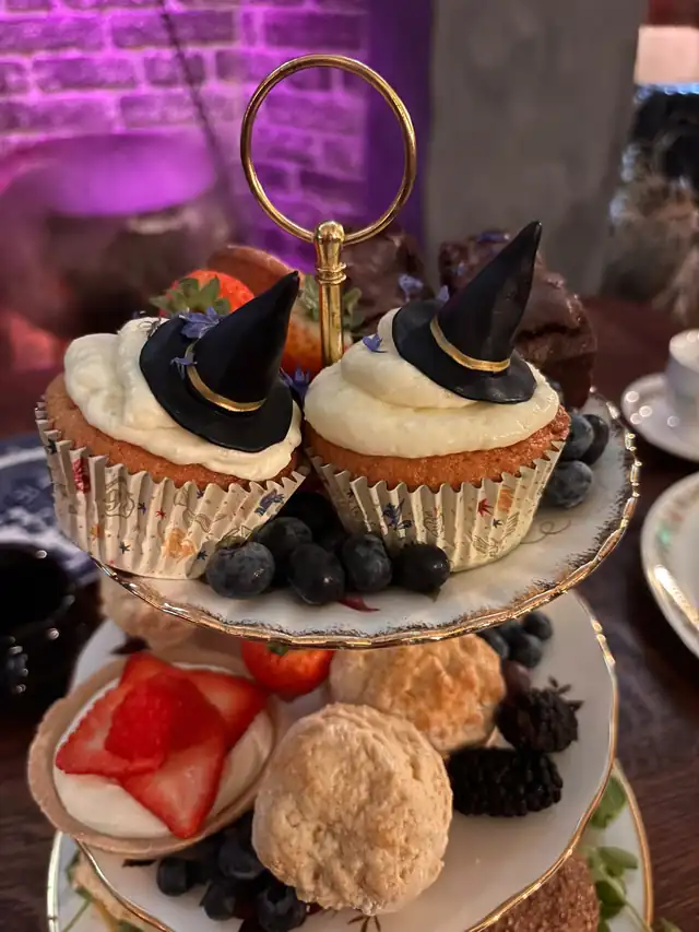 Witch-hat cupcakes with cream icing and berries, with scones and strawberry-topped treats below.