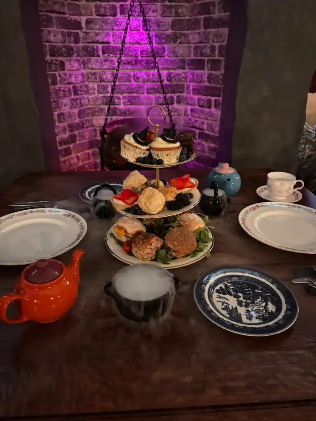 The Afternoon Wizard Tea table with a tiered stand, colourful teapots and a misting cauldron by the fireplace.